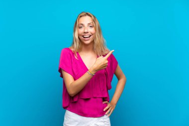 Izole mavi arka plan üzerinde Sarışın genç kadın şaşırttı ve yan işaret