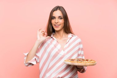 Genç kadın izole pembe duvar üzerinde bir pizza tutan gururlu ve kendini memnun