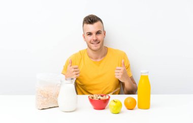 Genç sarışın adam jest kadar bir başparmak veren kahvaltı yapıyor