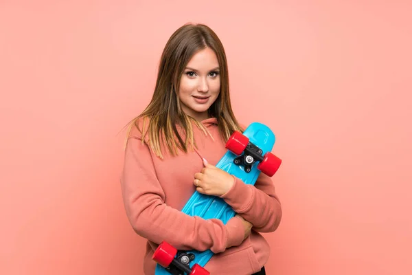 Menina adolescente com skate sobre fundo rosa isolado — Fotografia de Stock