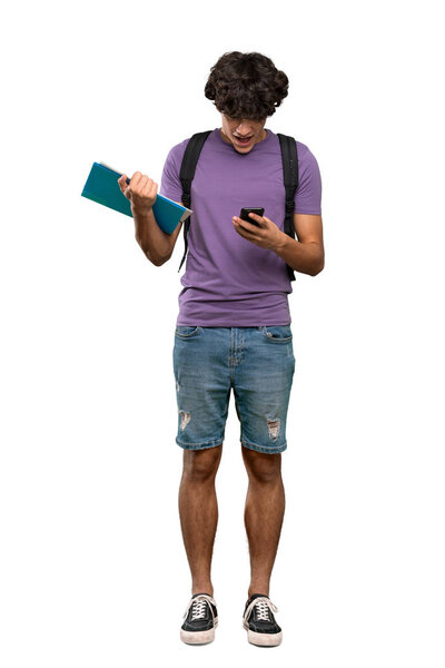 A full-length shot of a Young student man surprised and sending a message over isolated white background