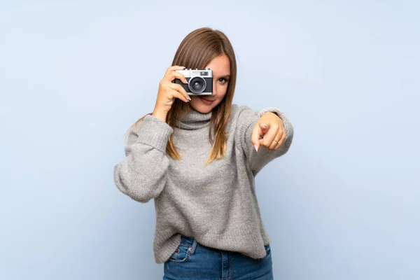 カメラを保持している孤立した青い背景の上にセーターを持つティーンエイジャーの女の子 — ストック写真