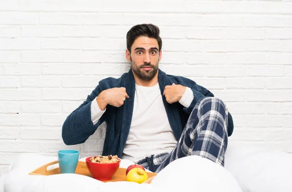 Man in bed with dressing gown and having breakfast with surprise facial expression