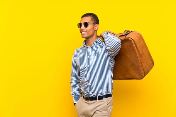 Hombre morena sosteniendo un maletín vintage sobre fondo amarillo aislado —  Fotos de Stock