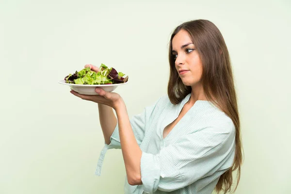 Mujer joven con ensalada sobre pared verde aislada — Foto de Stock