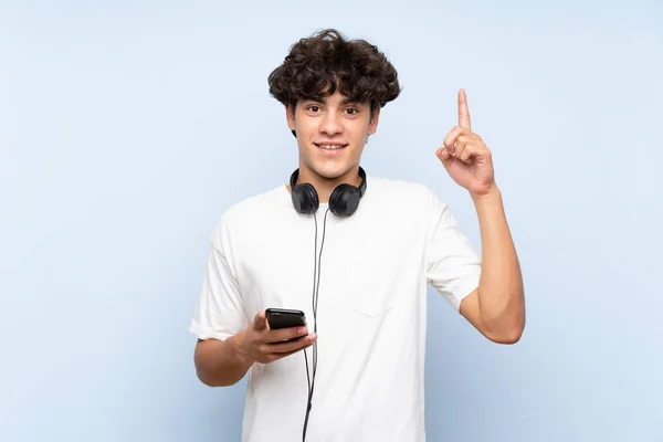 Young Man Listening Music Mobile Isolated Blue Wall Pointing Great — Φωτογραφία Αρχείου