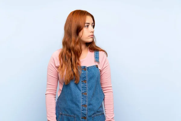 Teenager Redhead Girl Overalls Isolated Blue Background Looking Side — Stock Photo, Image