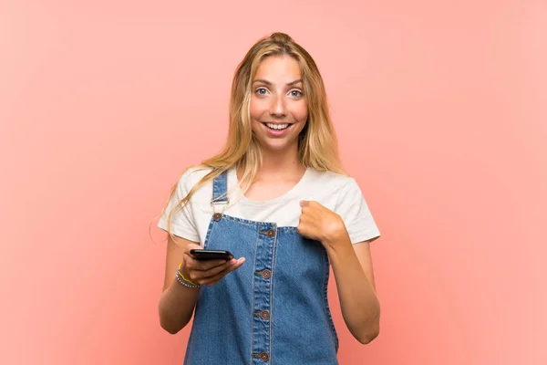 Blonde Jonge Vrouw Met Een Mobiele Telefoon Geïsoleerde Roze Muur — Stockfoto