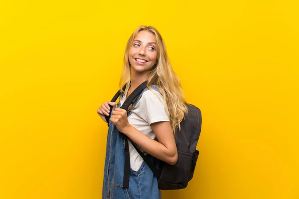 バックパックと孤立した黄色の背景の上にブロンドの若い女性 — ストック写真