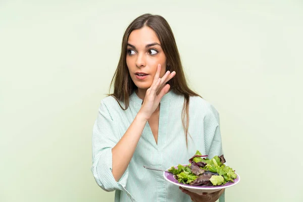 Mujer Joven Con Ensalada Sobre Una Pared Verde Aislada Susurrando — Foto de Stock