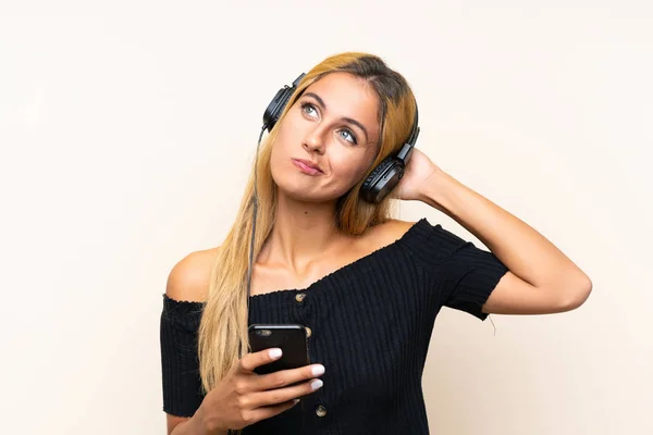 Молодая блондинка слушает музыку с мобильного на изолированном фоне — стоковое фото