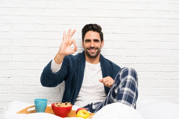 Hombre Cama Con Bata Desayunando Mostrando Signo Con Los Dedos —  Fotos de Stock
