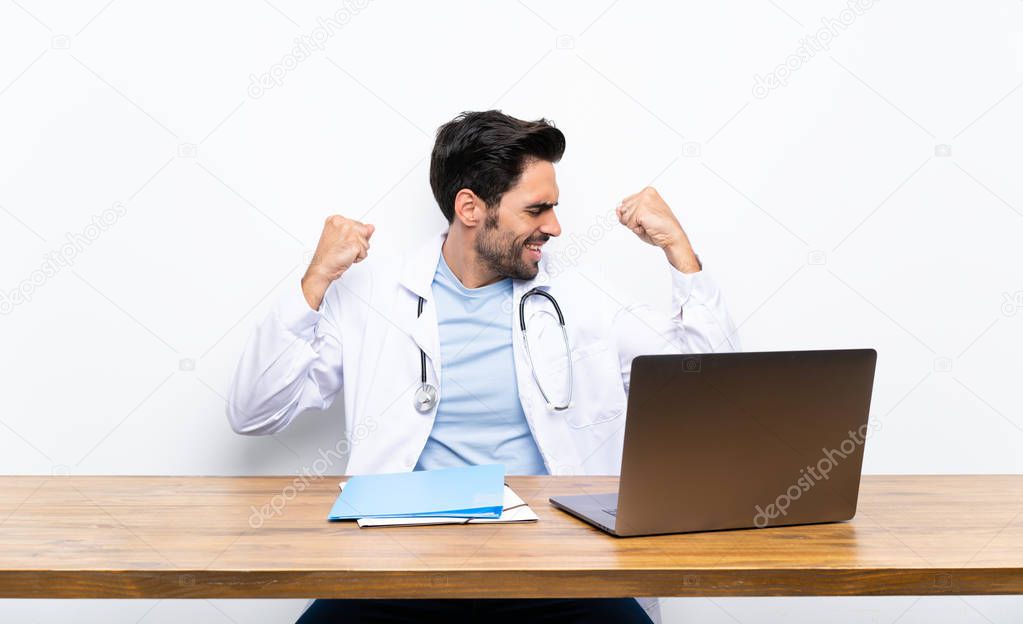 Young doctor man with his laptop over isolated wall celebrating a victory