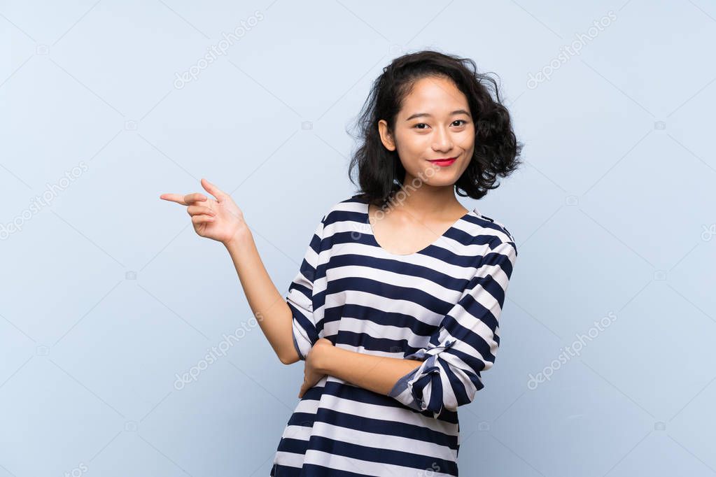 Asian young woman over isolated blue background pointing finger to the side