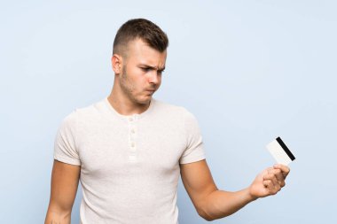 Bir kredi kartı tutan izole mavi arka plan üzerinde Genç yakışıklı sarışın adam