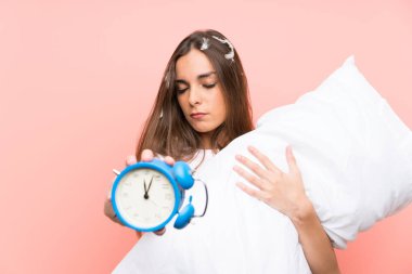 Vintage saat tutan izole pembe arka plan üzerinde pijama genç kadın