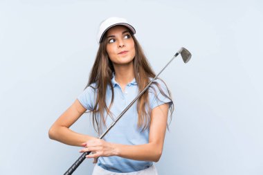Genç golfçü kadın izole mavi duvar üzerinde gülümseyerek yukarı bakıyor