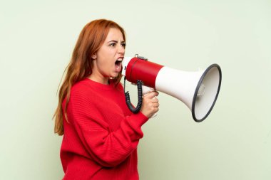 Bir megafon ile bağırarak izole yeşil arka plan üzerinde kazak ile genç redhead kız