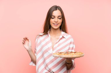Genç kadın izole pembe duvar üzerinde bir pizza tutan çok gülümsüyor