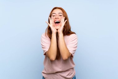 Izole mavi arka plan üzerinde Genç redhead kız bağırarak ve bir şey ilan