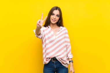 Sarı arka planda genç bir kadın gülümsüyor ve zafer işareti gösteriyor.