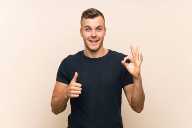 Izole arka plan üzerinde ok işareti ve başparmak kadar jest gösteren genç yakışıklı sarışın adam