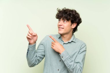İşaret parmağı ile işaret izole yeşil duvar üzerinde genç adam harika bir fikir
