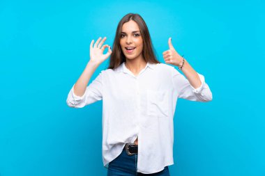 İzole edilmiş mavi arka plan üzerinde genç bir kadın işaret ve işaret işareti gösteriyor.