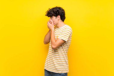 Ağız kapsayan izole sarı duvar üzerinde genç adam ve yan bakıyor