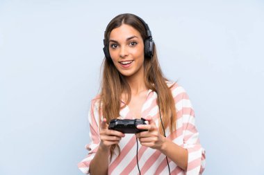 İzole mavi duvar üzerinde bir video oyunu denetleyicisi ile oynayan genç kadın