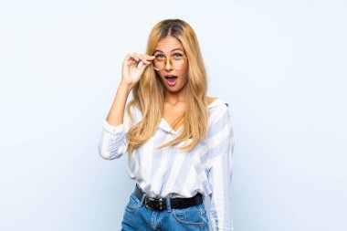 Gözlük lü izole mavi arka plan üzerinde genç sarışın kadın ve şaşırttı