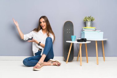 Genç bir kadın yerde oturuyor. Davet edildiği için ellerini yana açıyor.