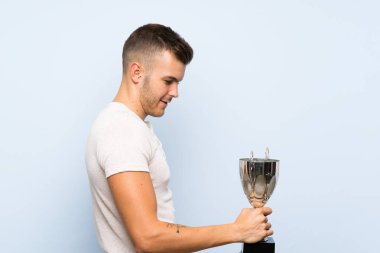 Bir kupa tutan izole mavi arka plan üzerinde Genç yakışıklı sarışın adam
