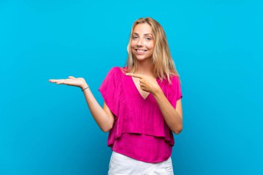 Bir reklam eklemek için avuç üzerinde copyspace hayali tutan izole mavi arka plan üzerinde Blonde genç kadın