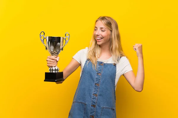 Mujer Joven Rubia Sobre Fondo Amarillo Aislado Sosteniendo Trofeo —  Fotos de Stock