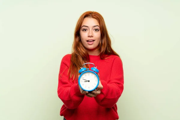ヴィンテージ目覚まし時計を保持する孤立した緑の背景の上にセーターを持つティーンエイジャー赤毛の女の子 — ストック写真