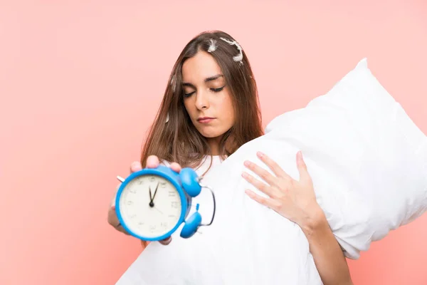 Giovane donna in pigiama su sfondo rosa isolato con orologio vintage — Foto Stock