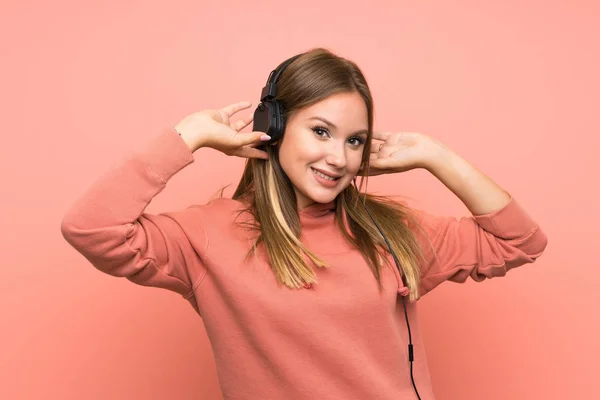 Teenager girl listening music over isolated pink background — Stock Photo, Image