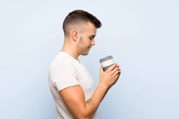 Joven Guapo Hombre Rubio Sobre Aislado Fondo Azul Sosteniendo Taza —  Fotos de Stock