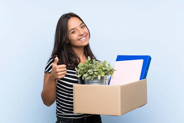 Young brunette girl making a move while picking up a box full of things with thumbs up because something good has happened