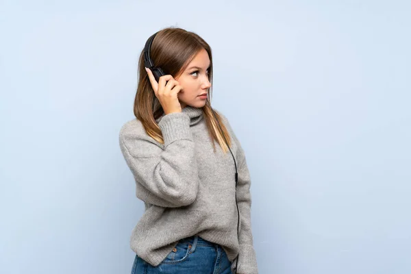 Chica Adolescente Con Suéter Sobre Fondo Azul Aislado Escuchando Música — Foto de Stock