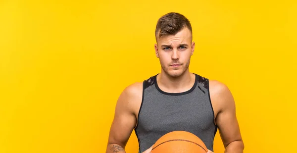 Young handsome blonde man holding a basket ball over isolated yellow background