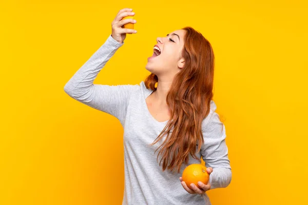 Adolescente pelirroja chica sosteniendo un naranja sobre aislado amarillo fondo —  Fotos de Stock