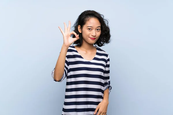 指でOkサインを示す孤立した青い背景の上にアジアの若い女性 — ストック写真