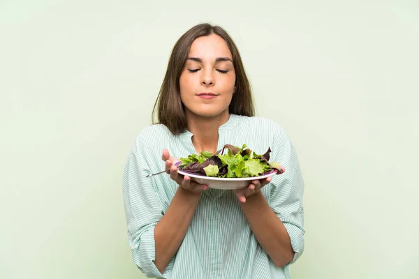 Young woman with salad over isolated green wall