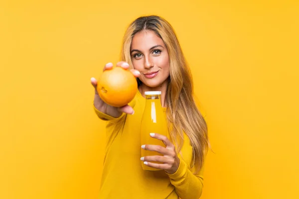 Молодая блондинка держит апельсиновый сок на желтом фоне — стоковое фото
