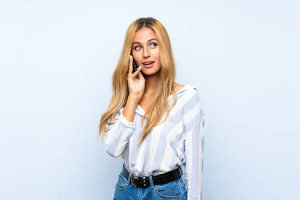 Mladá Blondýnka Izolovaném Modrém Pozadí Která Udržuje Rozhovor Mobilním Telefonem — Stock fotografie