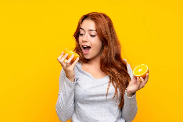 Adolescente ruiva menina segurando uma laranja sobre fundo amarelo isolado — Fotografia de Stock