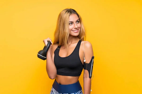 Fiatal sport nő, hogy a súlyemelés a kettlebell keresztül elszigetelt sárga háttér — Stock Fotó