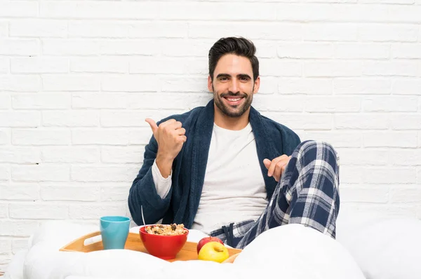 Man in bed with dressing gown and having breakfast pointing to the side to present a product